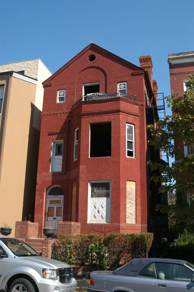 Red brick house with empty windows and boarded entrances.