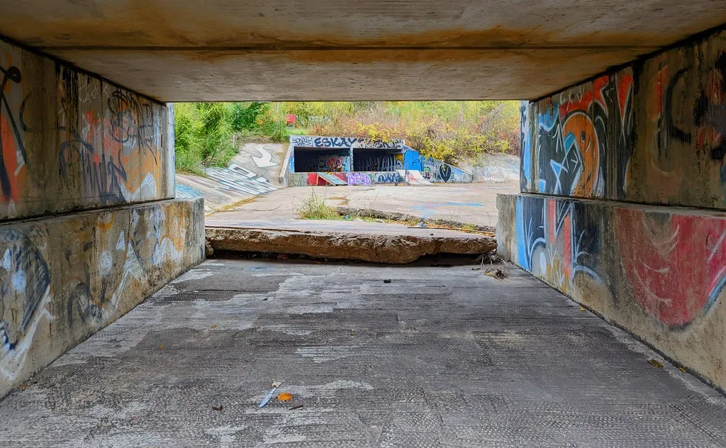 Passage en béton graffité donnant sur un canal à sec.