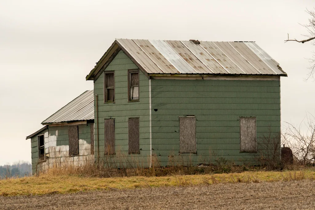 Two-storey green house with boarded windows and a weathered metal roof.