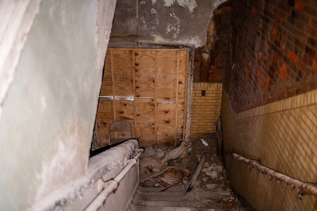 Stairway strewn with debris beneath a boarded opening.