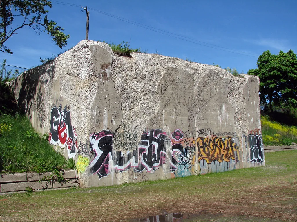 Massive graffitied concrete remnant with broken edges and a grassy top in a green space.