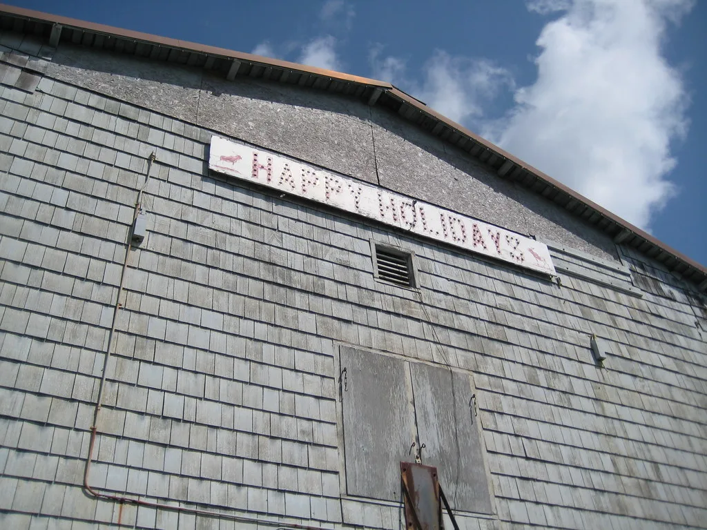 Grey shingled gable with a boarded opening and old sign.