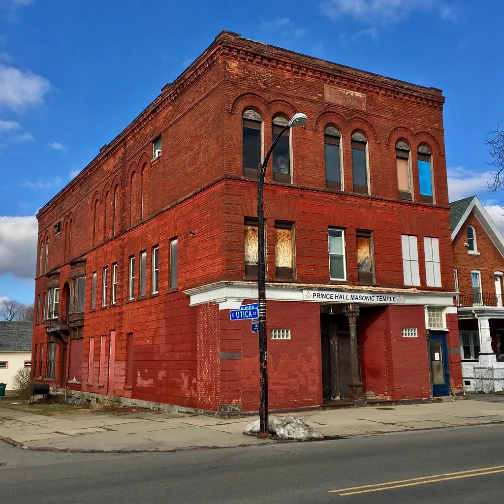 Ancien bâtiment rouge à l’angle d’une rue, aux ouvertures condamnées.