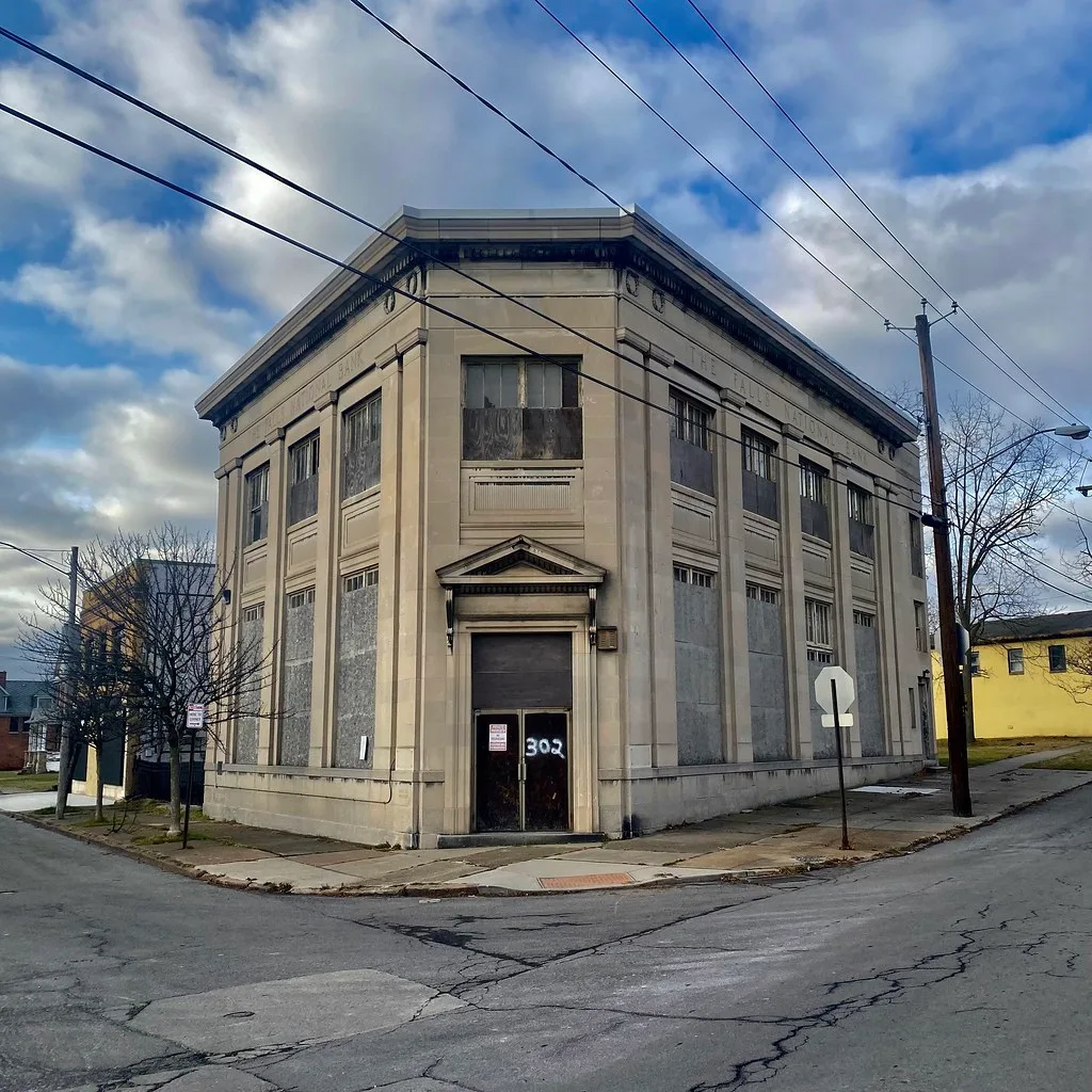 Abandoned former bank on a street corner with large boarded windows and a door marked 302.