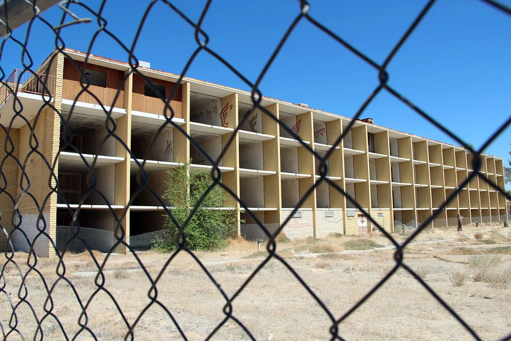 Old building with open bays and graffiti behind a wire fence.
