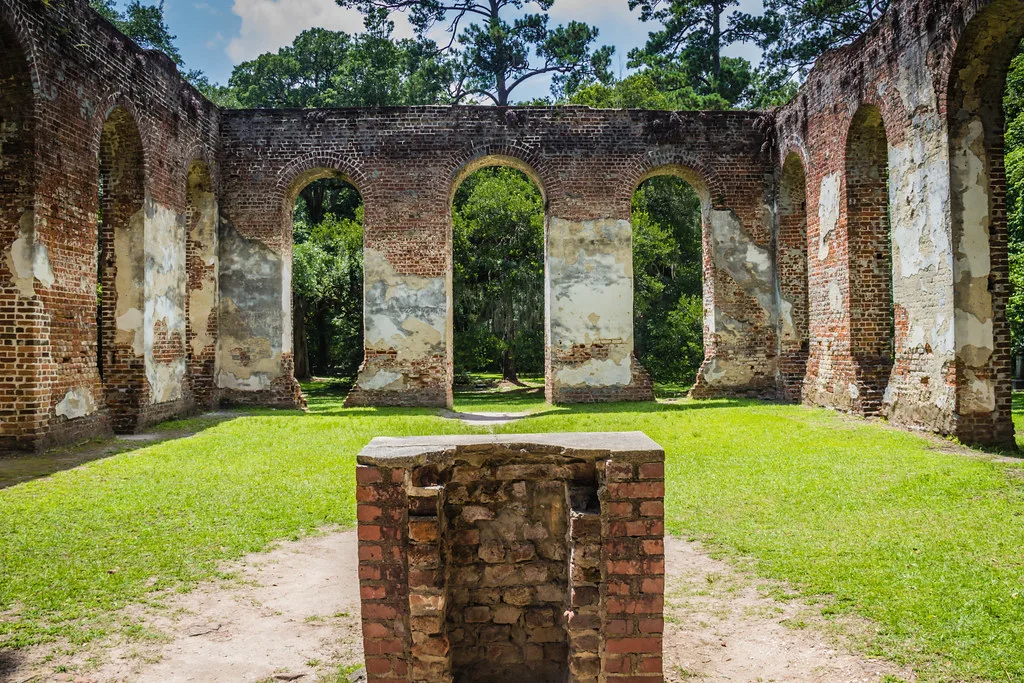 Ruined brick walls with large arched openings around a lawn.