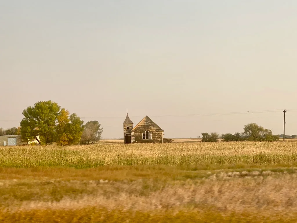 Old weathered wooden church amid a golden meadow.