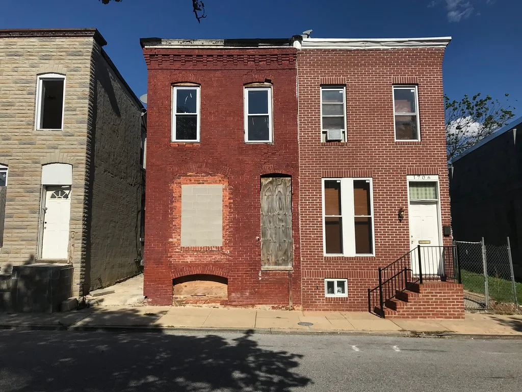 Maison de briques rouges aux ouvertures condamnées dans une rangée de maisons.