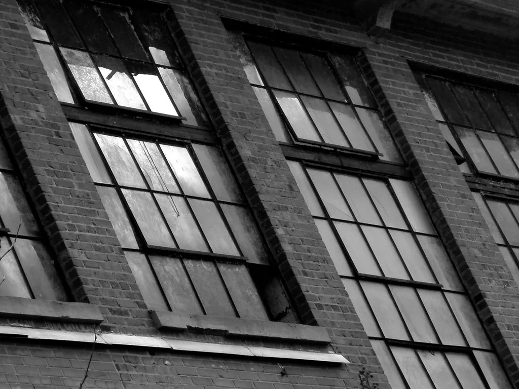 Large industrial windows with broken panes in a brick facade.