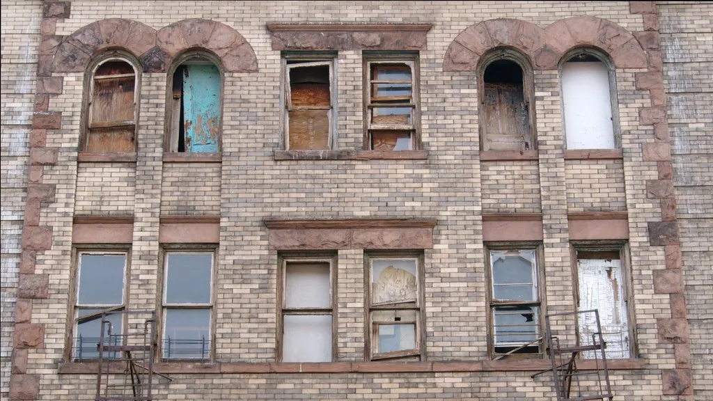 Pale brick facade with boarded windows and broken panes.