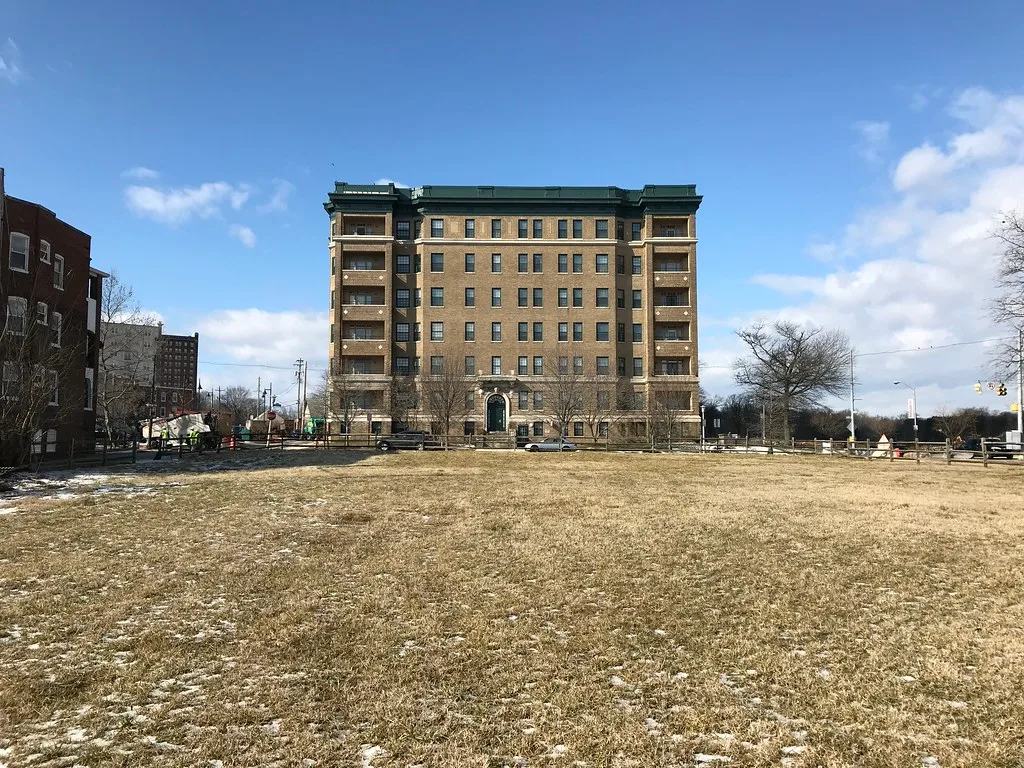 The Riviera building in Baltimore viewed beyond a vacant grassy lot.