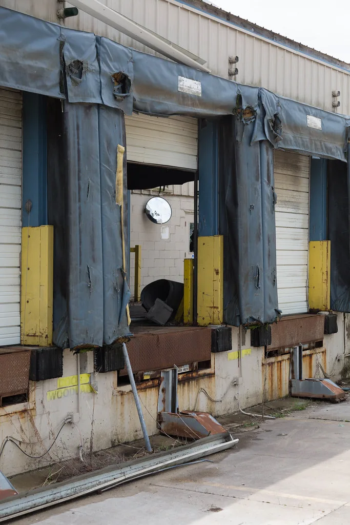 Abandoned loading bays with torn dock shelters, partly open doors and metal debris.