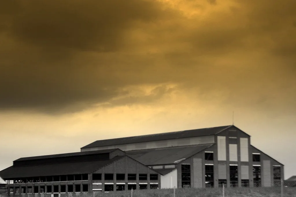 Old large shed with empty window openings beneath a dark sky.