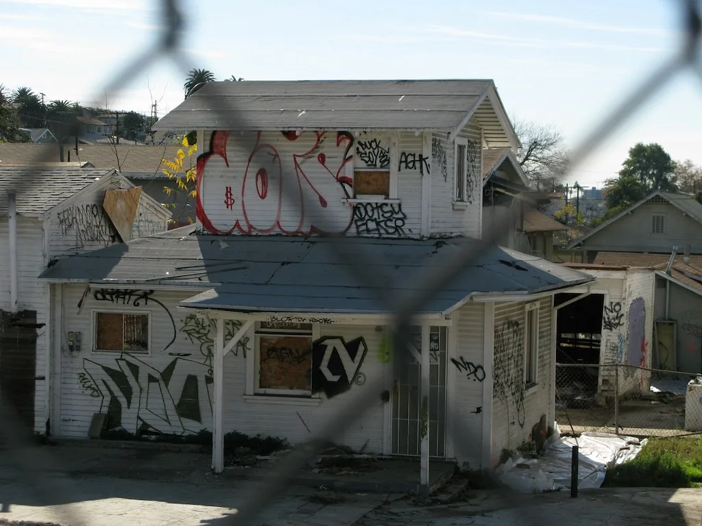Boarded white house covered in graffiti behind a fence.