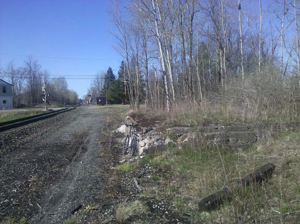 Remains of stone foundations among brush beside a railway track.