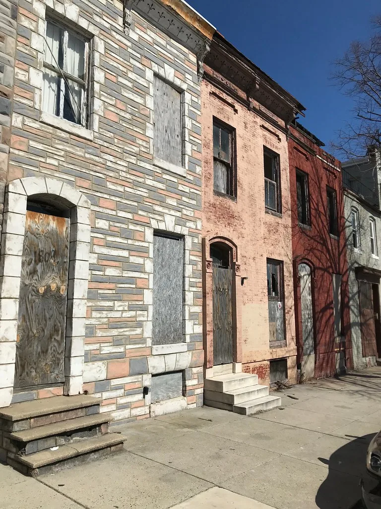 Rangée de maisons aux façades de pierre et de brique avec portes murées et fenêtres cassées.