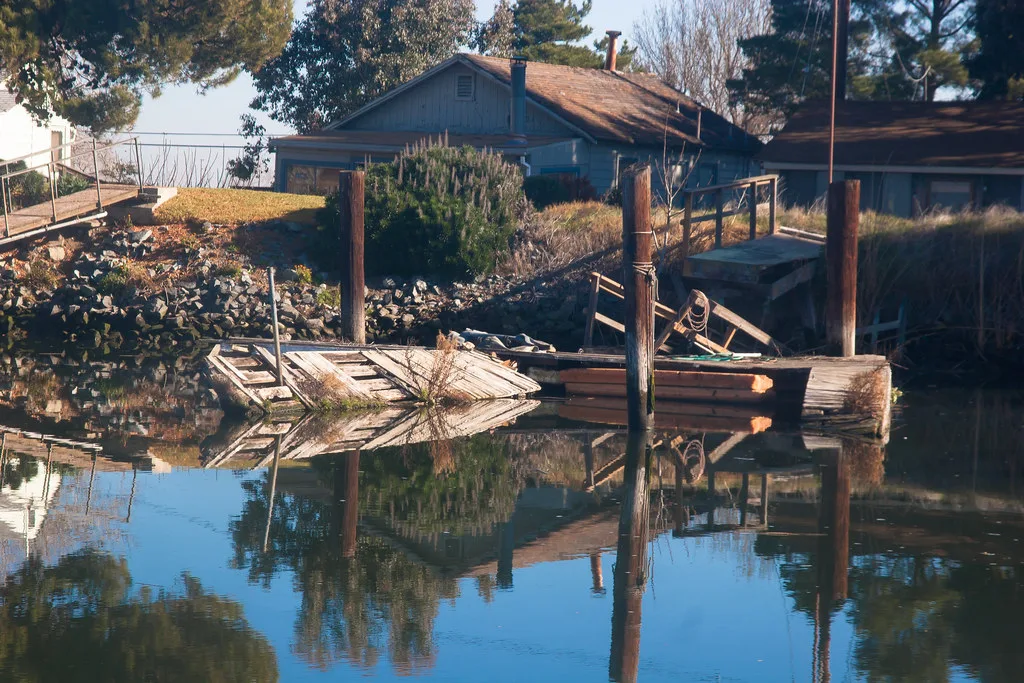 Abandoned wooden pier and collapsed walkway reflected in still water.