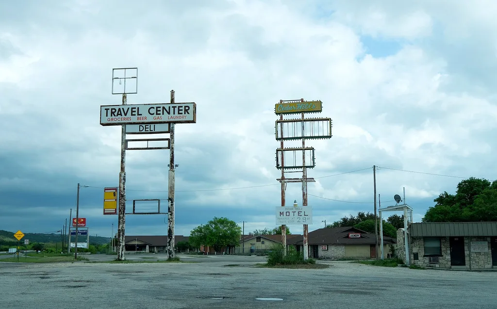 Ancien relais routier abandonné aux grands cadres d’enseignes vides devant un motel fermé et un parking désert.