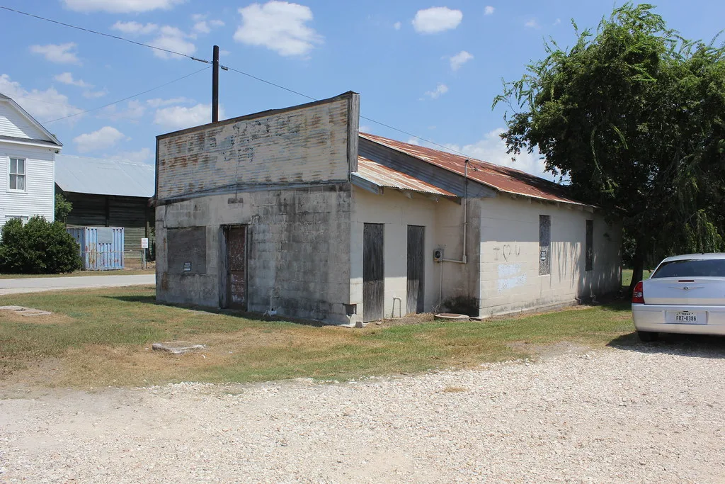 Ancien petit commerce maçonné aux ouvertures murées sous un toit de tôle rouillée.