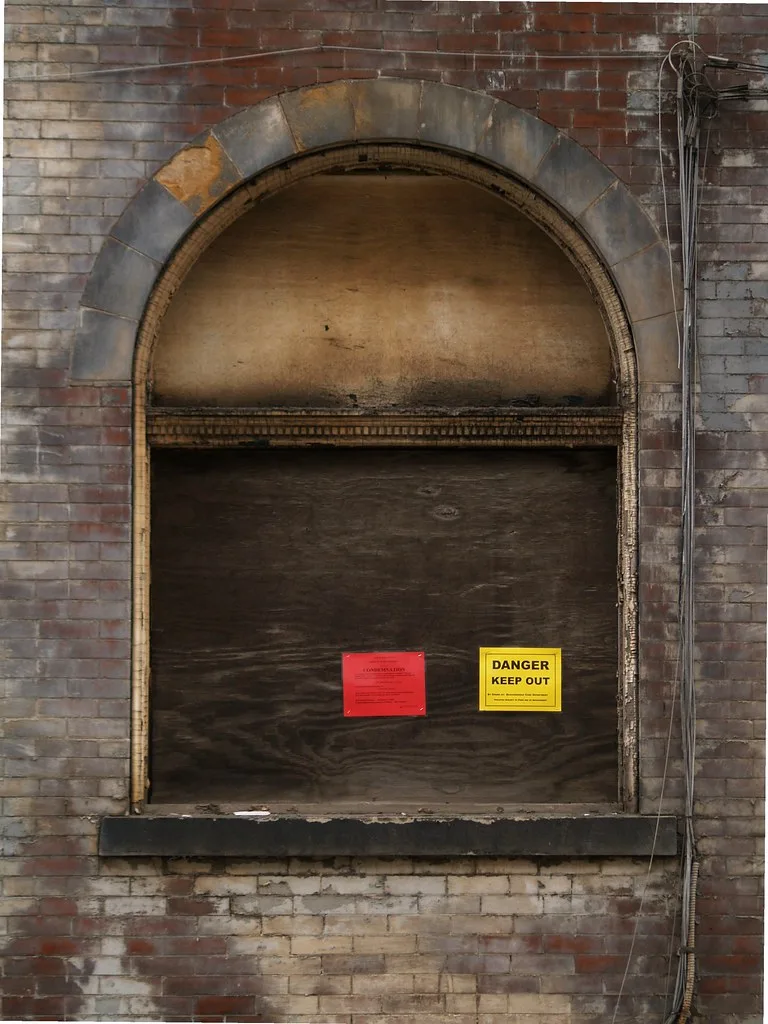 Fenêtre cintrée condamnée dans un mur de briques avec panneaux de danger.