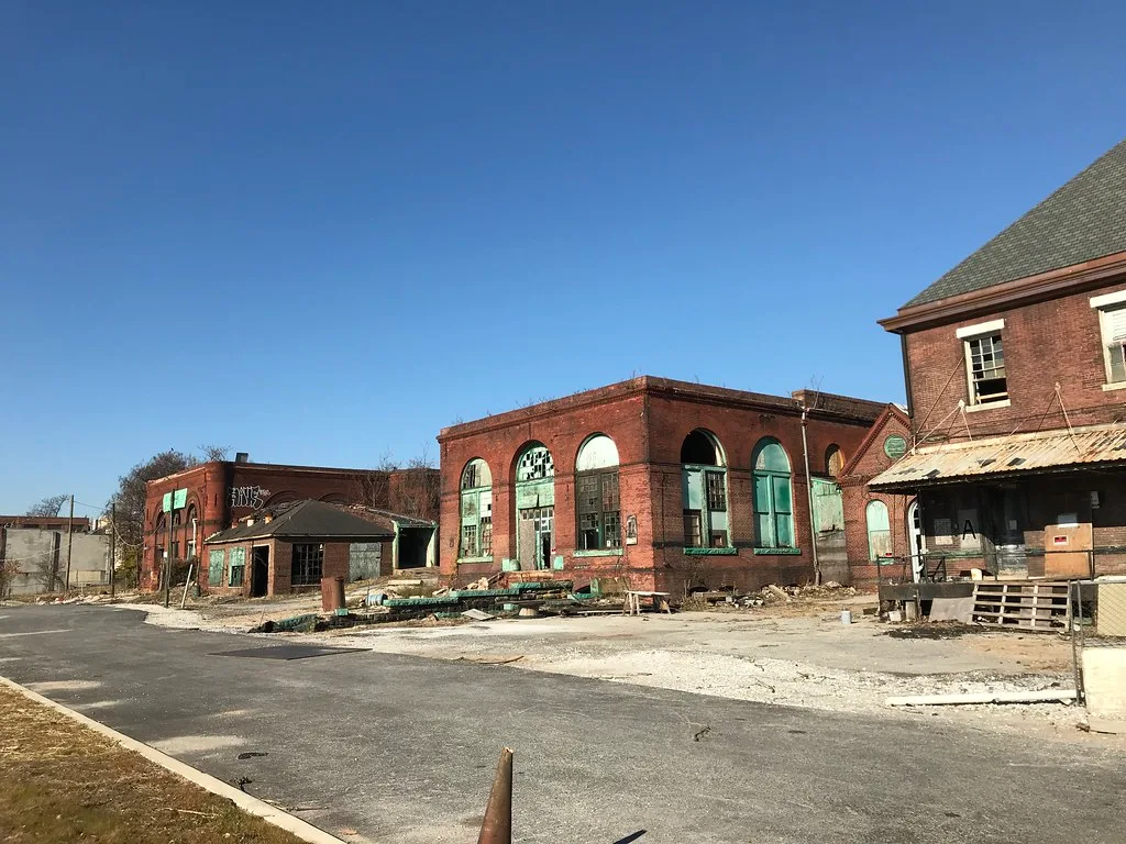 Abandoned red brick industrial complex with large broken or boarded arched openings, with deteriorated loading platforms and steps.