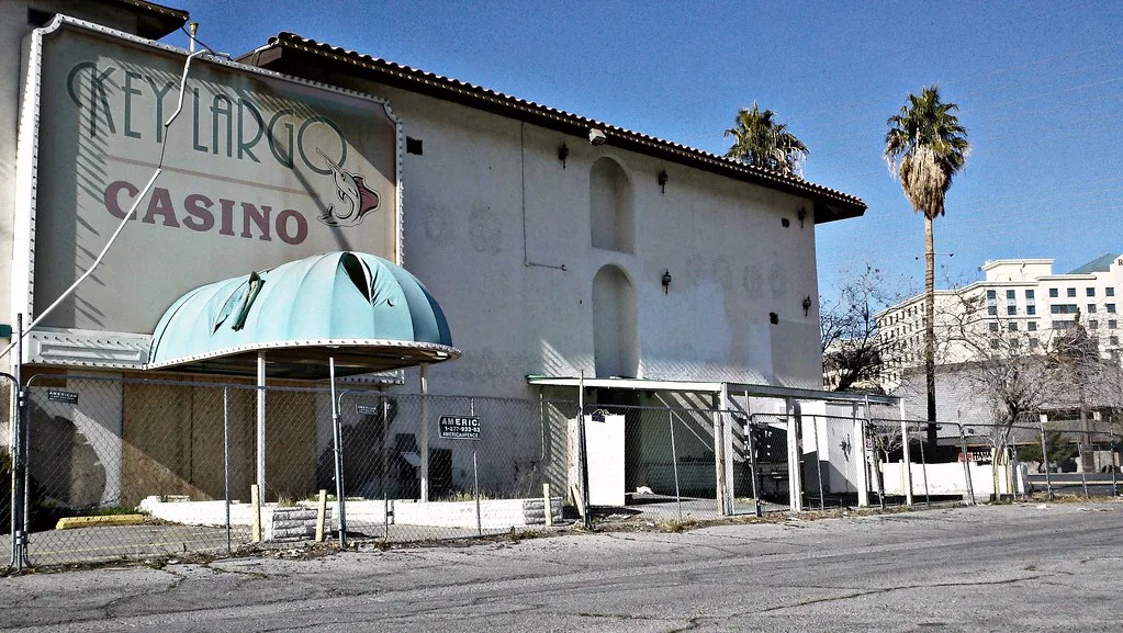 Fenced Key Largo Casino facade with a torn turquoise canopy and sealed openings.