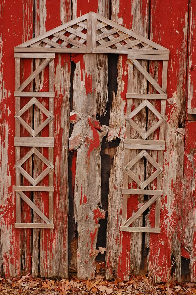 Wooden lattice against the decaying red siding of an outbuilding.