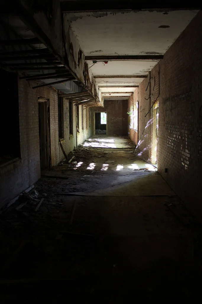 Couloir abandonné aux murs carrelés et plafond dégradé éclairé par les fenêtres.