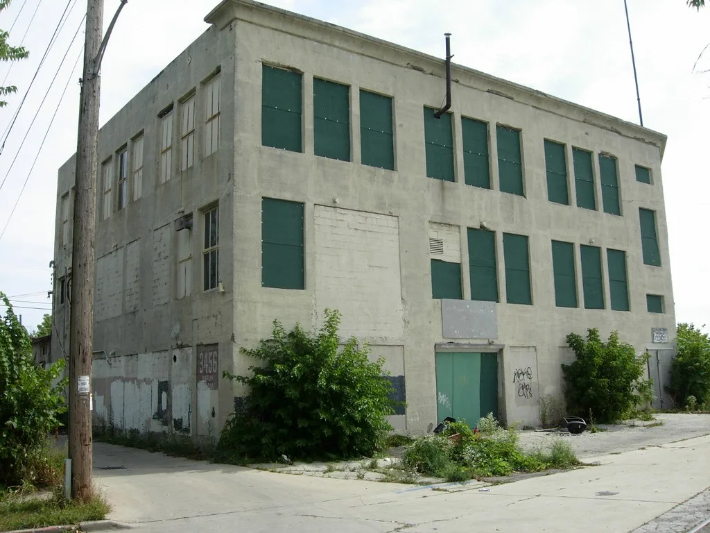 Abandoned building with green-boarded windows and overgrown surroundings.
