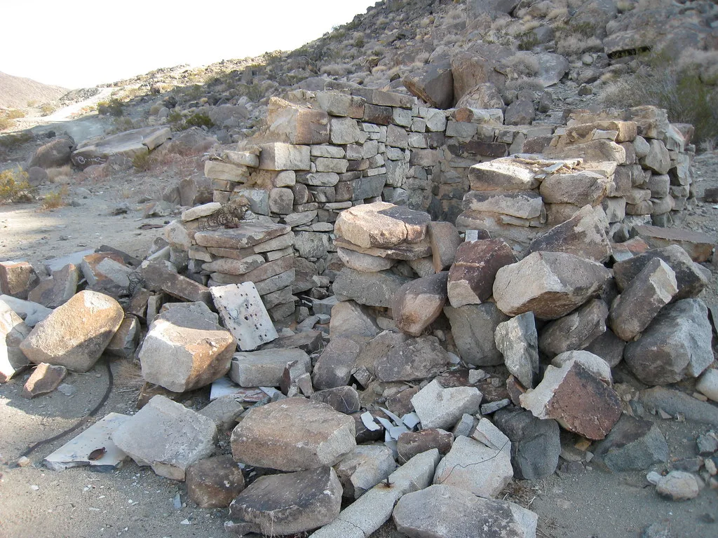 Abandoned ruin of a small stone structure, roofless and surrounded by fallen blocks on rocky ground.