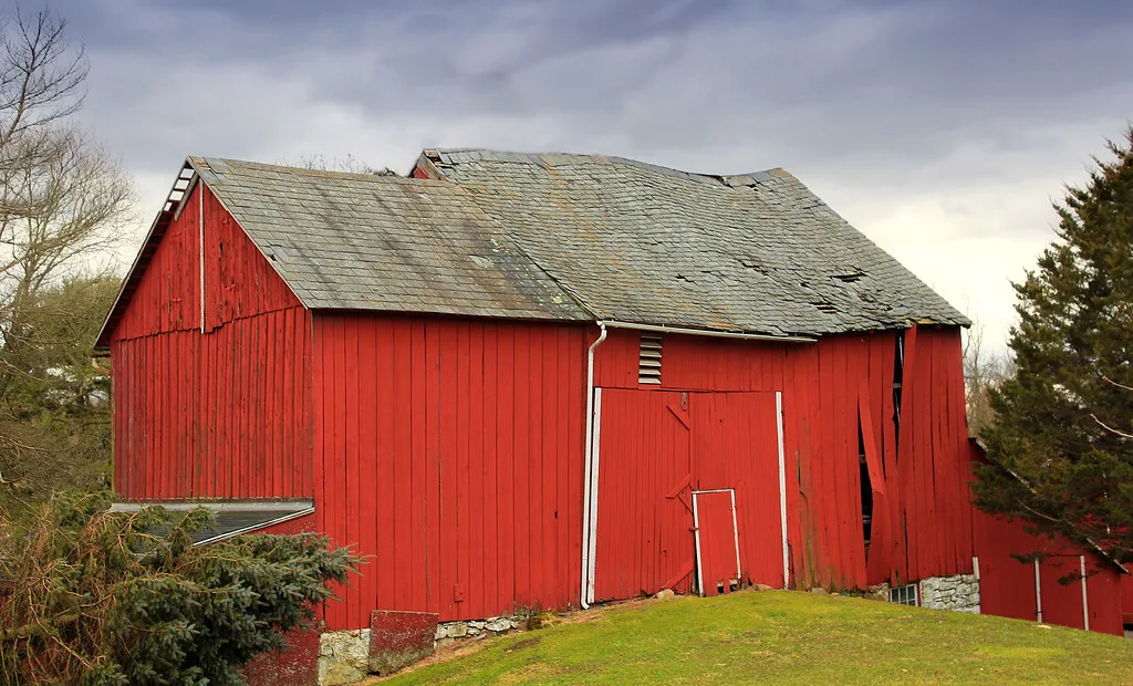 Decaying red barn with a sagging roof and separated boards.