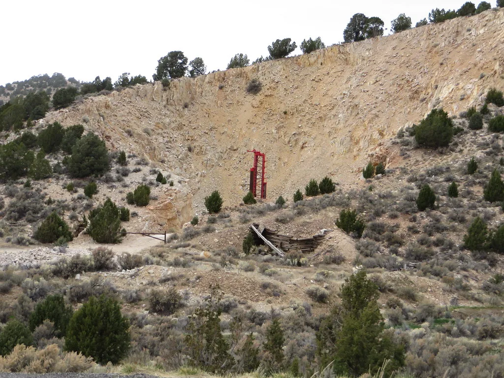 Remains of an abandoned installation in a rocky excavation, with a collapsed wooden structure and a red steel upright.