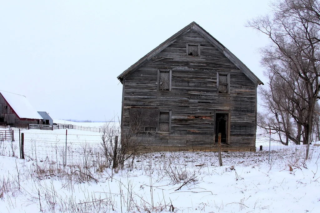 Dilapidated grey wooden building in a snowy field.