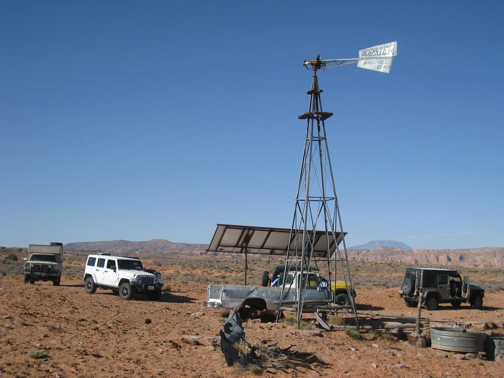 Ancienne pompe éolienne sans roue dans un terrain désertique avec des véhicules.