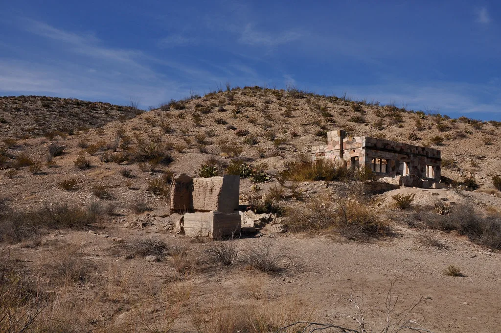 Vestiges abandonnés de murs et piliers de maçonnerie sur une pente désertique couverte de broussailles.