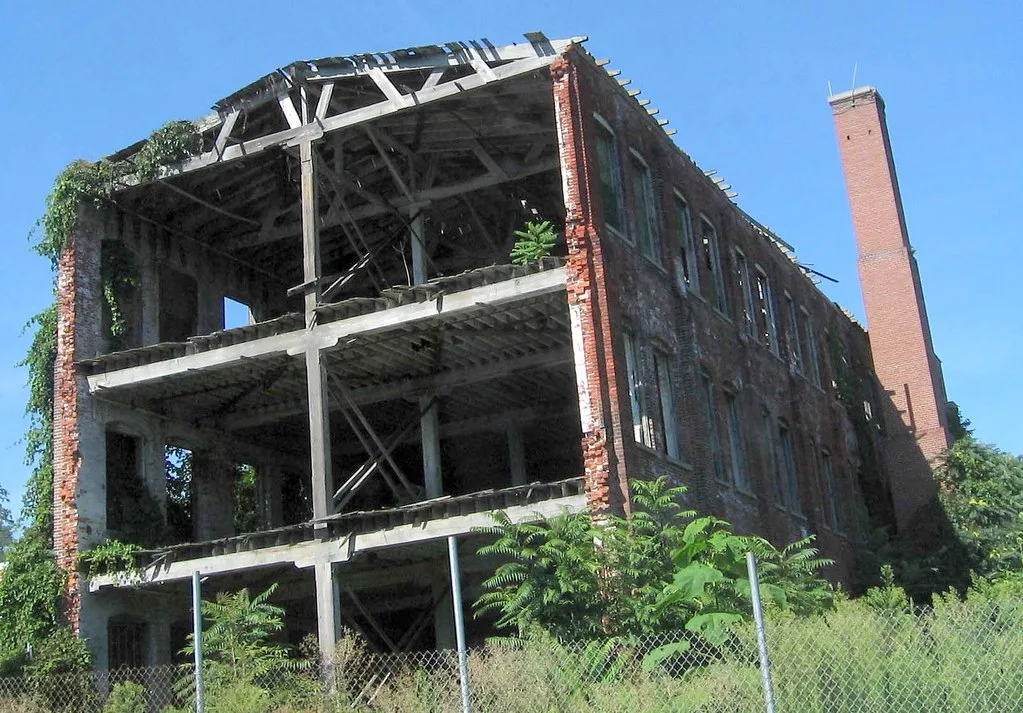 Brick industrial building torn open across several floors, with exposed beams and ivy.