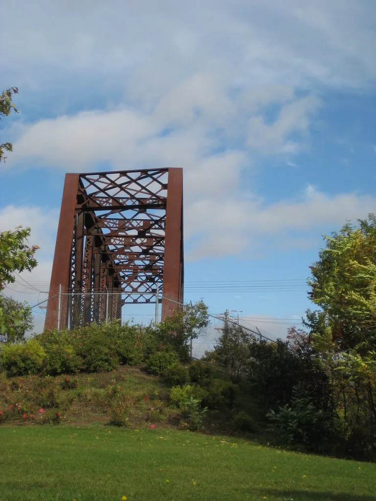 Ancien pont métallique derrière une clôture et des broussailles.