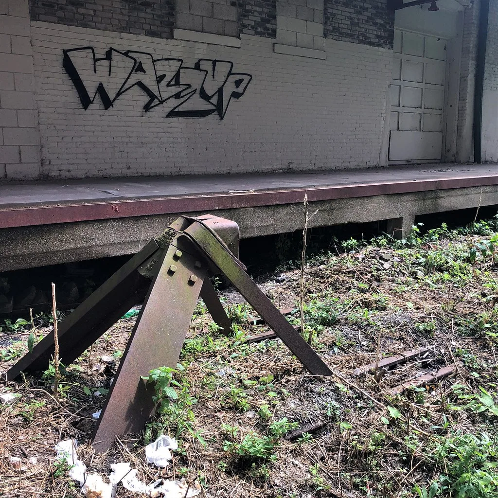 Rusty railway buffer stop in grass in front of an old loading platform.