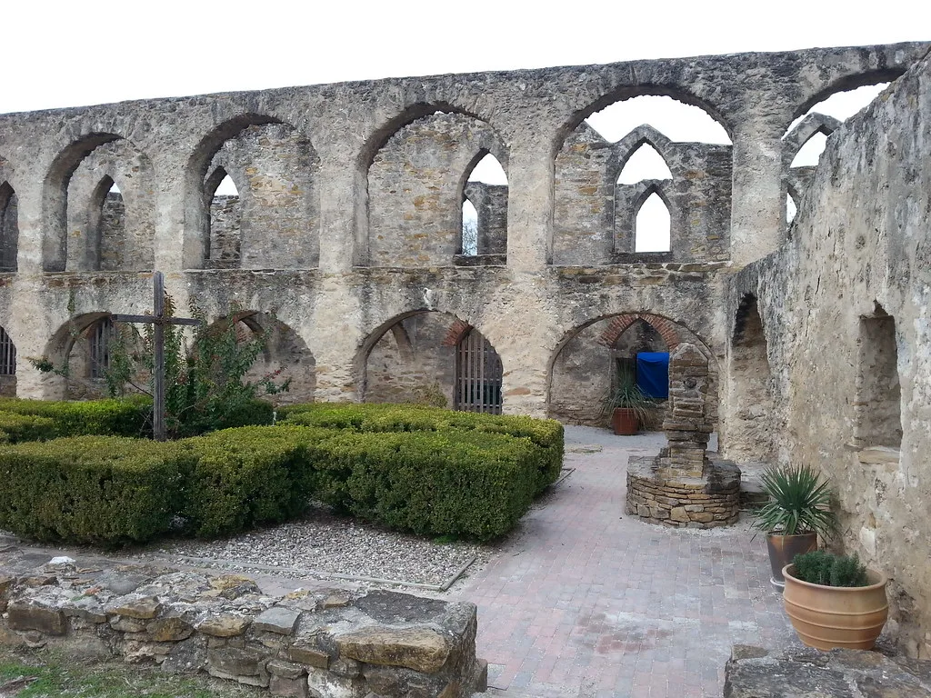 Ruined stone walls with two levels of arches around a garden.