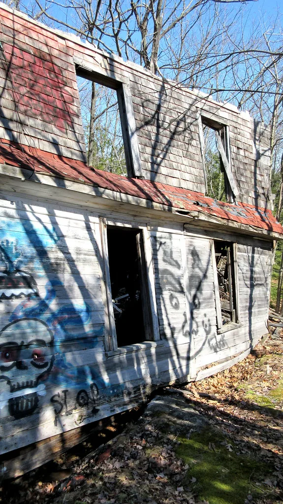 Ruines d’une maison en bois taguée aux fenêtres vides, dans les arbres.