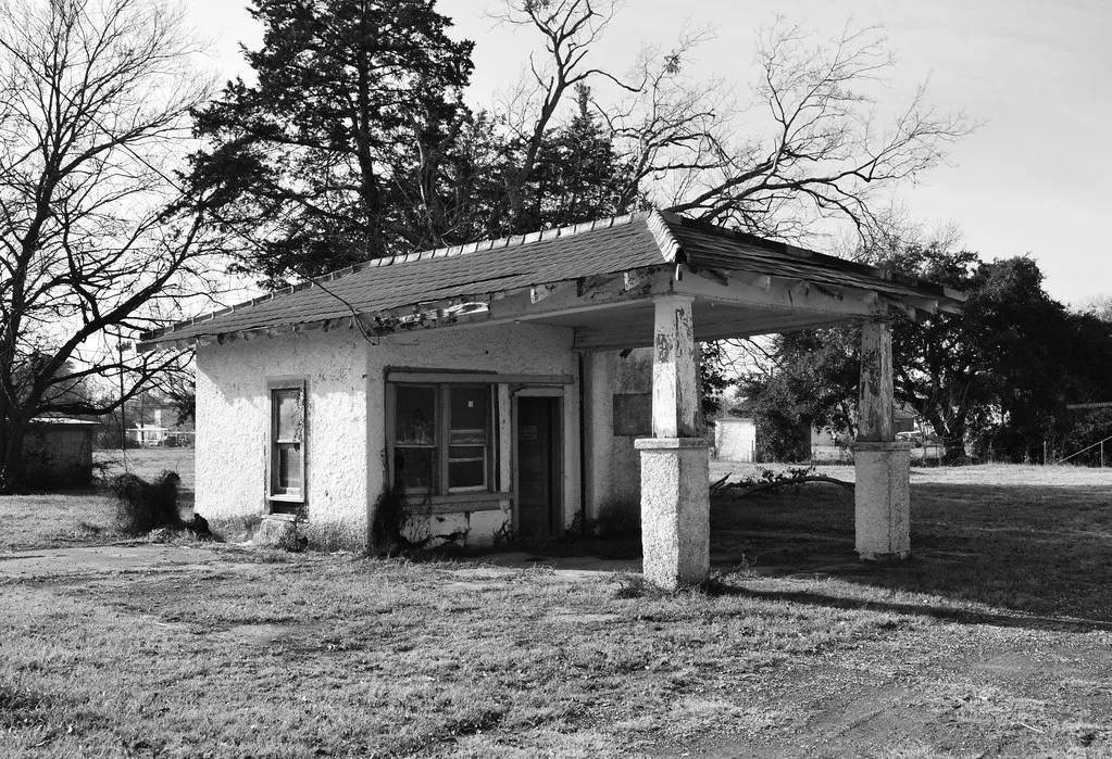 Small neglected petrol station with a two-pillar canopy and peeling white facade.