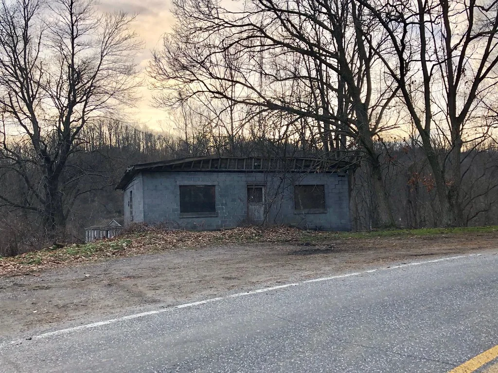 Old small building with boarded windows beside a road.
