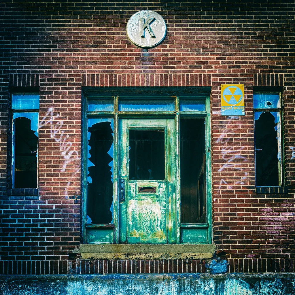 Peeling green door and broken windows in a brick facade.