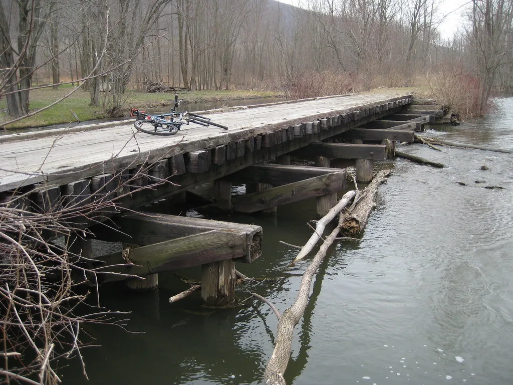 Ancien pont en bois au tablier partiellement manquant au-dessus de l’eau.