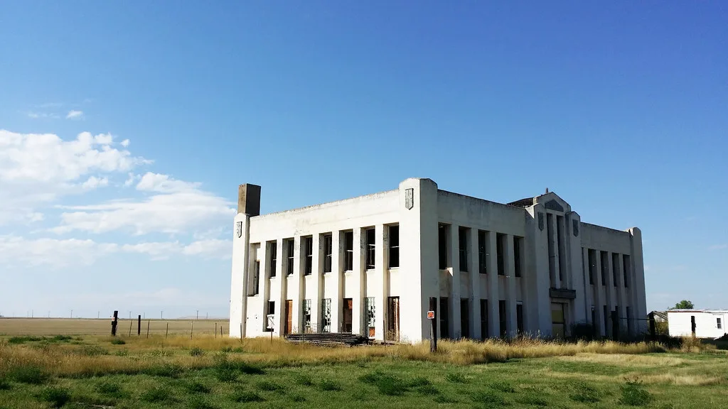 Old white building with tall unglazed windows in a meadow.
