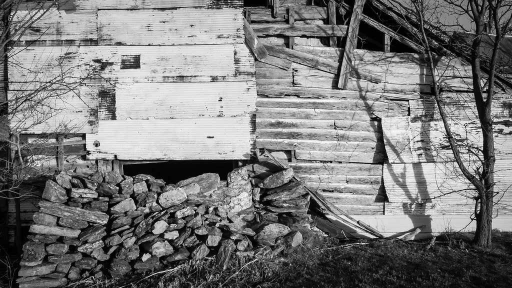 Partially torn wooden wall above a collapsed stone foundation.