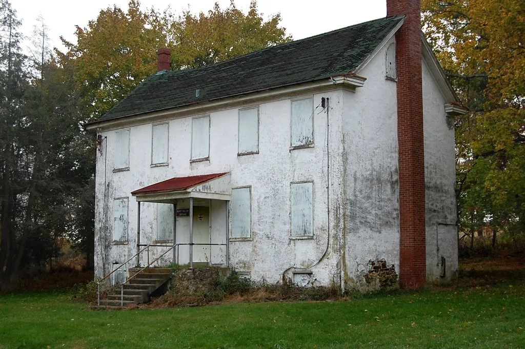 Old white house with boarded windows.