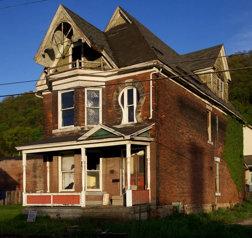 Brick house with ornate gables, broken windows and a dilapidated porch.