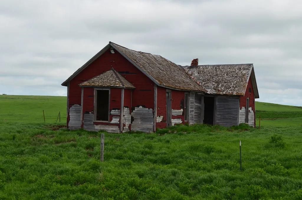 Small dilapidated red and grey house in a meadow.