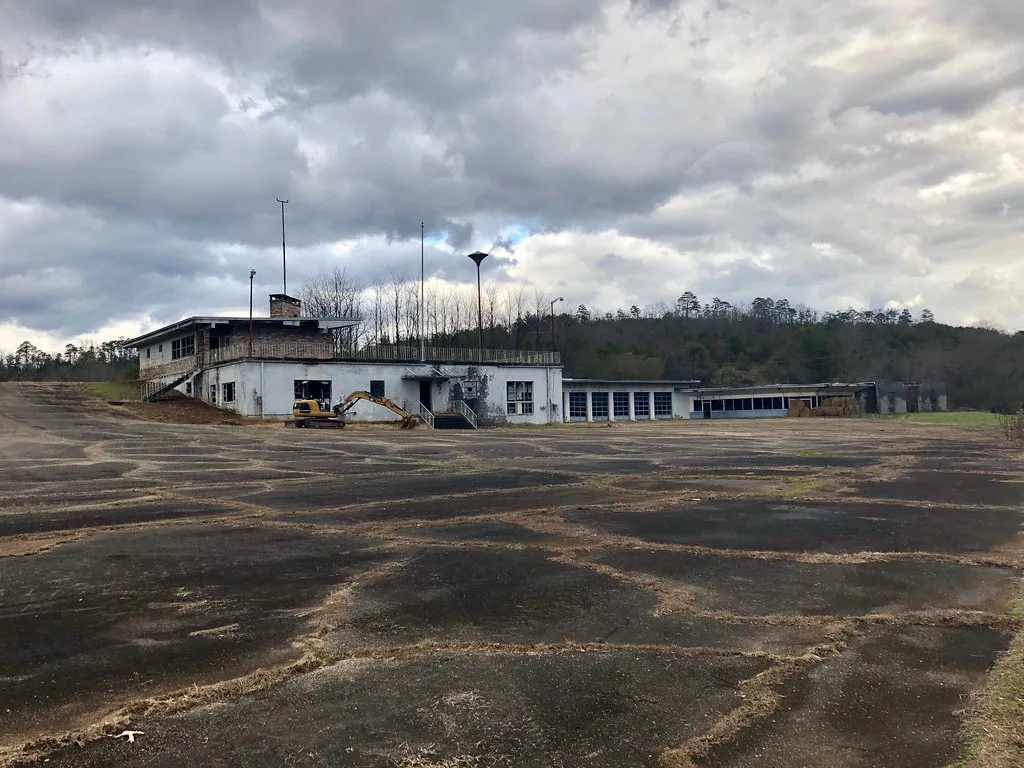 Long dilapidated white building and former terrace facing a broad cracked asphalt surface.